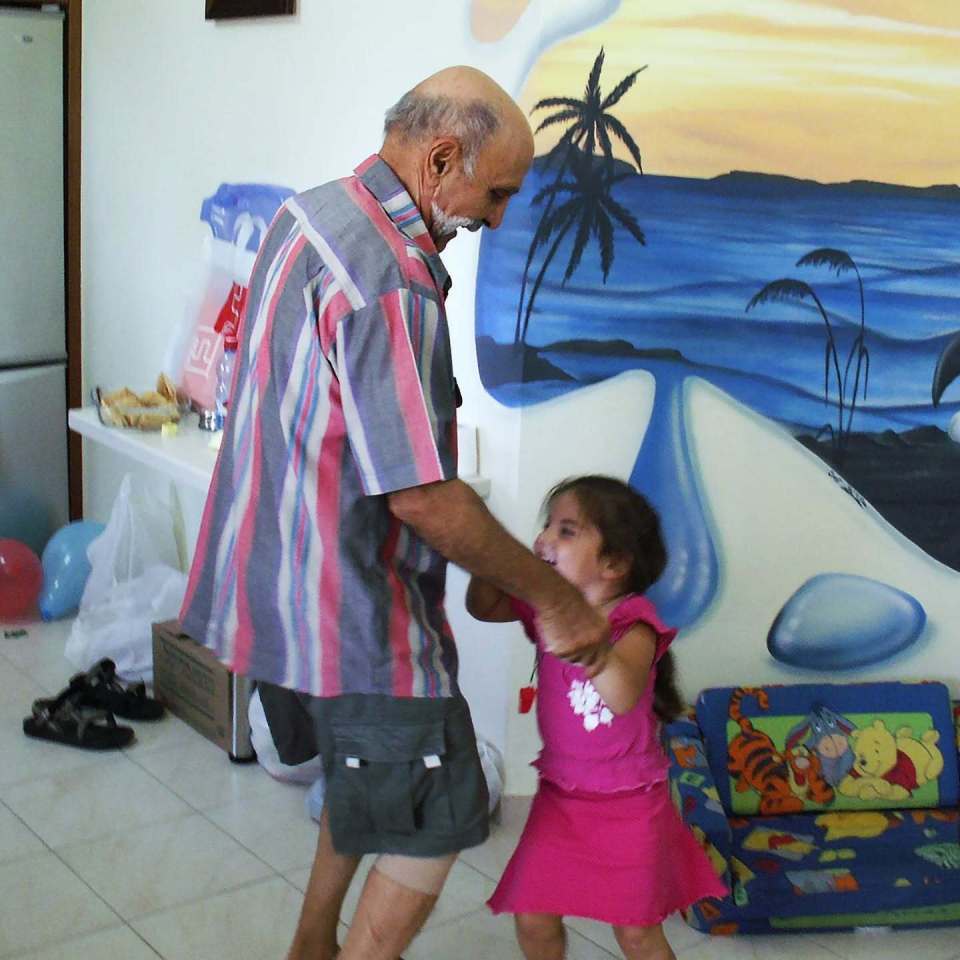 An elderly man and a young girl dancing in front of a beach mural.