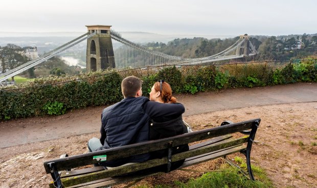 Couple sitting on a bench overlooking the Clifton Suspension Bridge.