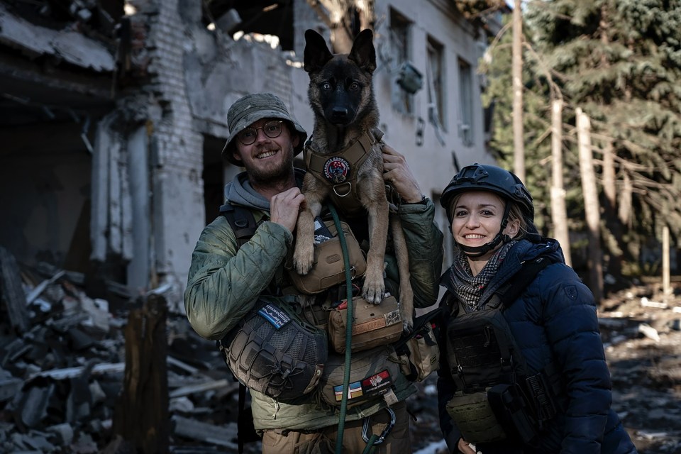 British humanitarian worker Edward Scott with a dog and another aid worker amidst war-torn buildings in Ukraine.