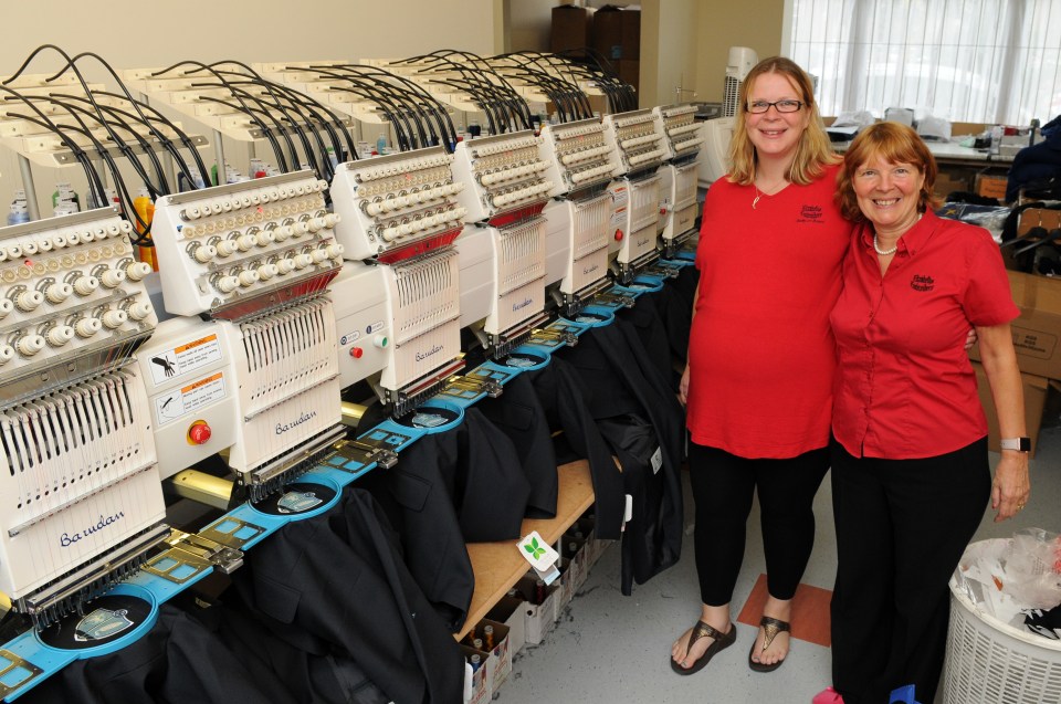 Two women standing in front of embroidery machines.