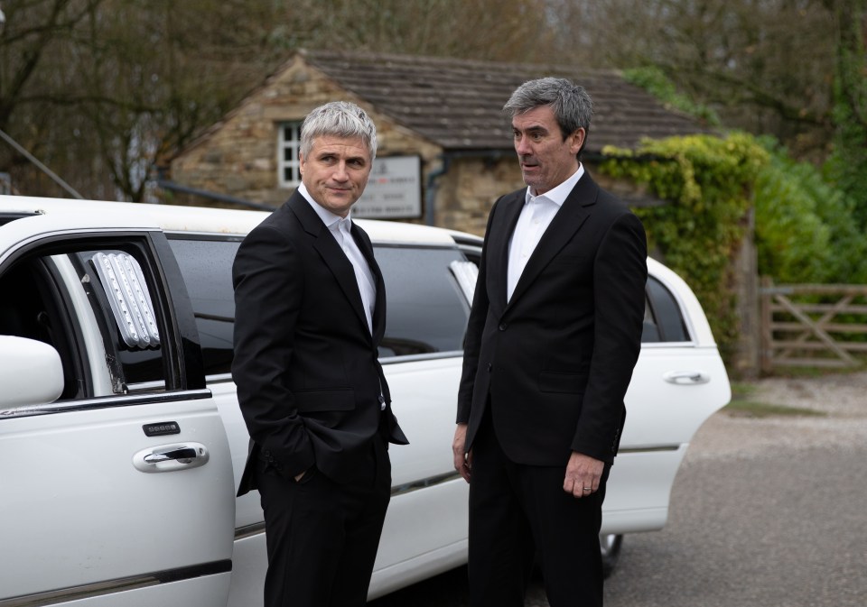 Two men in suits standing by a white limousine.