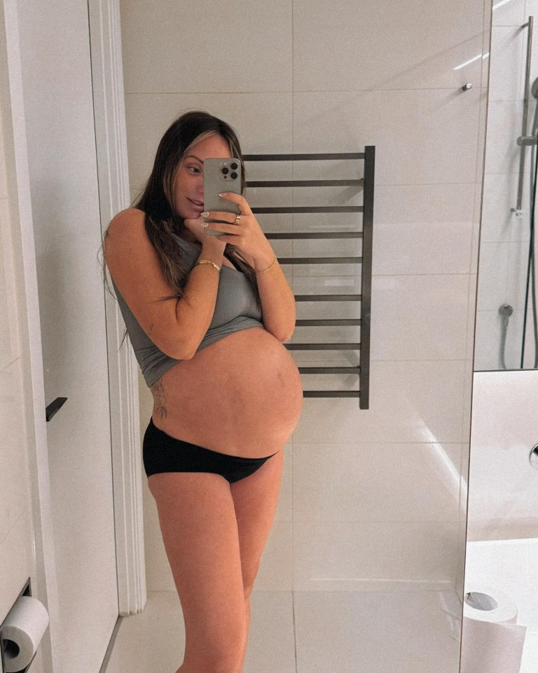 Pregnant woman taking a selfie in a bathroom mirror.