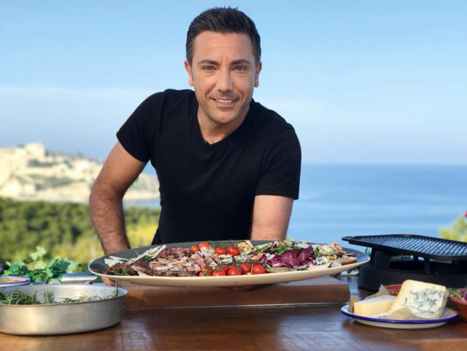 Chef Gino D'Acampo holding a platter of grilled meat and vegetables.