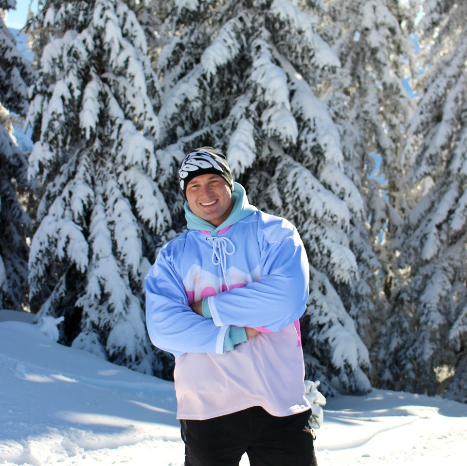 Man in winter hockey jersey standing in snowy woods.