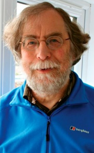 Portrait of a man with glasses and a beard wearing a blue jacket.