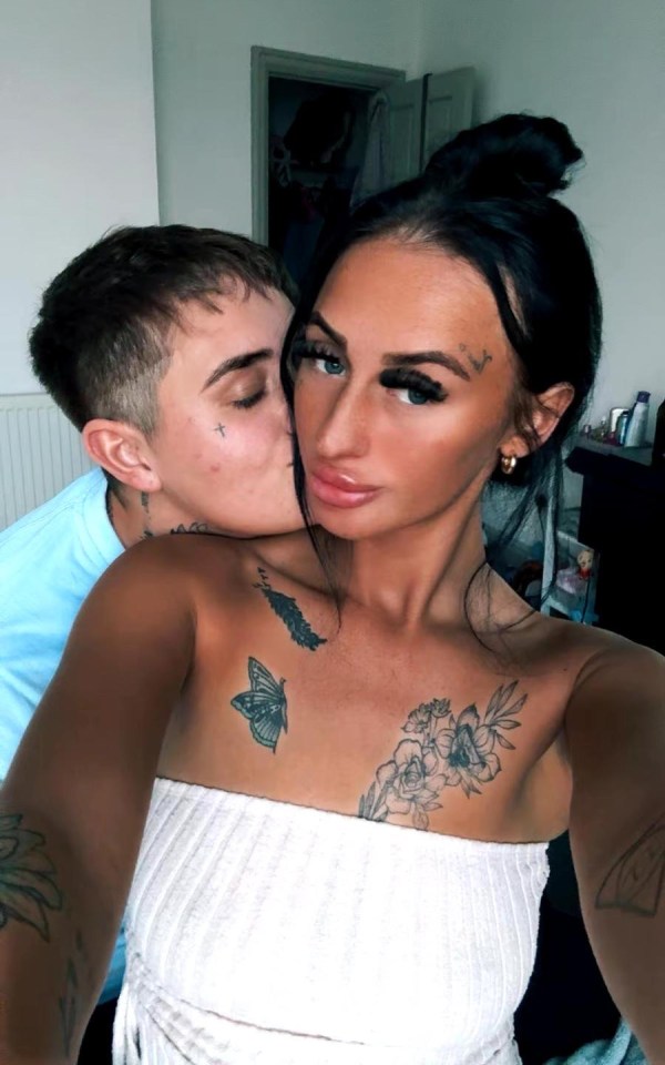 Photo of a couple embracing; the woman has several tattoos on her chest.