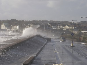 Waves crashing against a seawall near buildings.