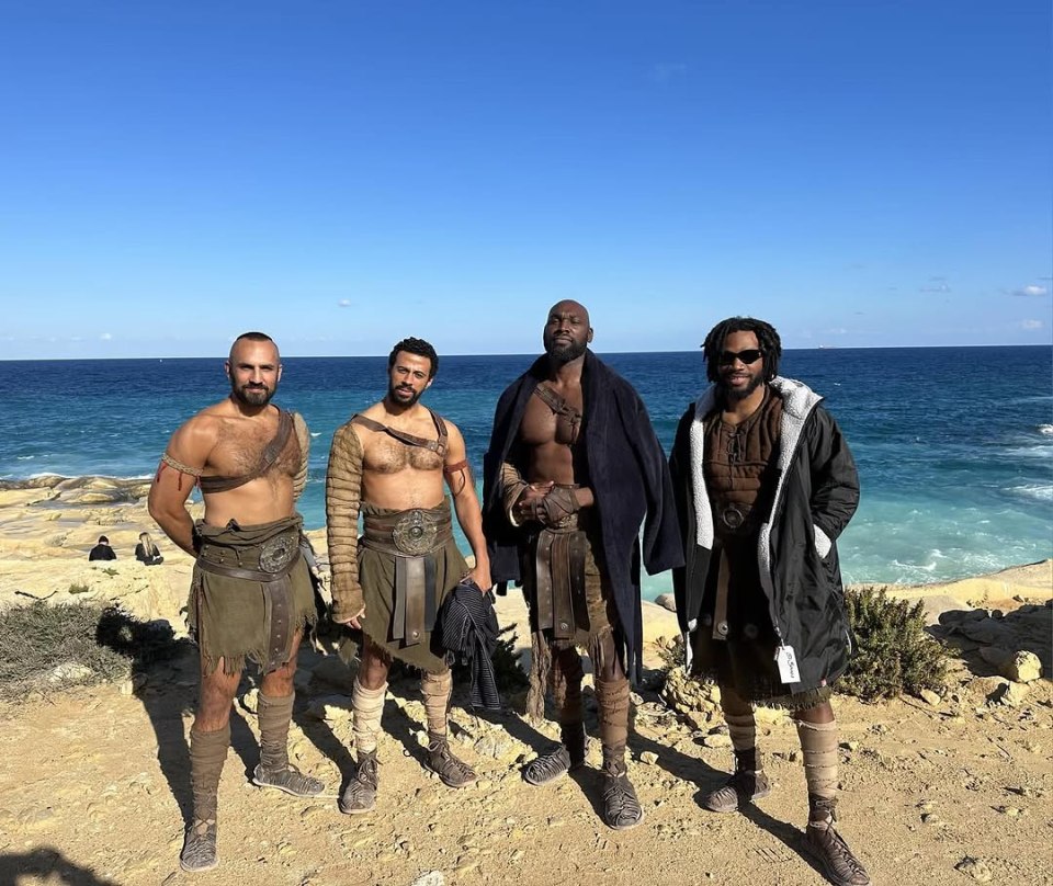 Four actors in Gladiator costumes on a beach.