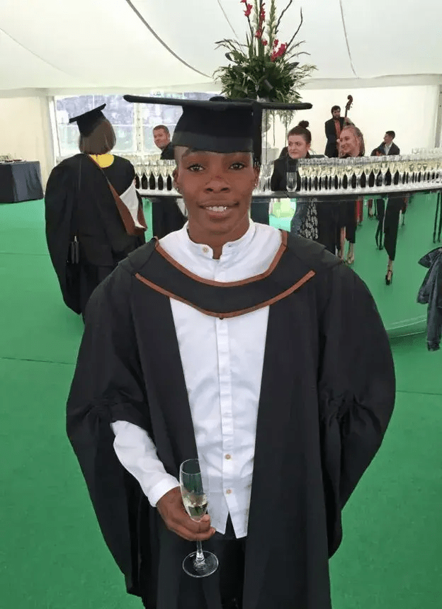 Graduate in cap and gown holding a glass of champagne.