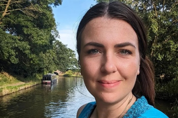 Woman in teal top by canal with boat in background.