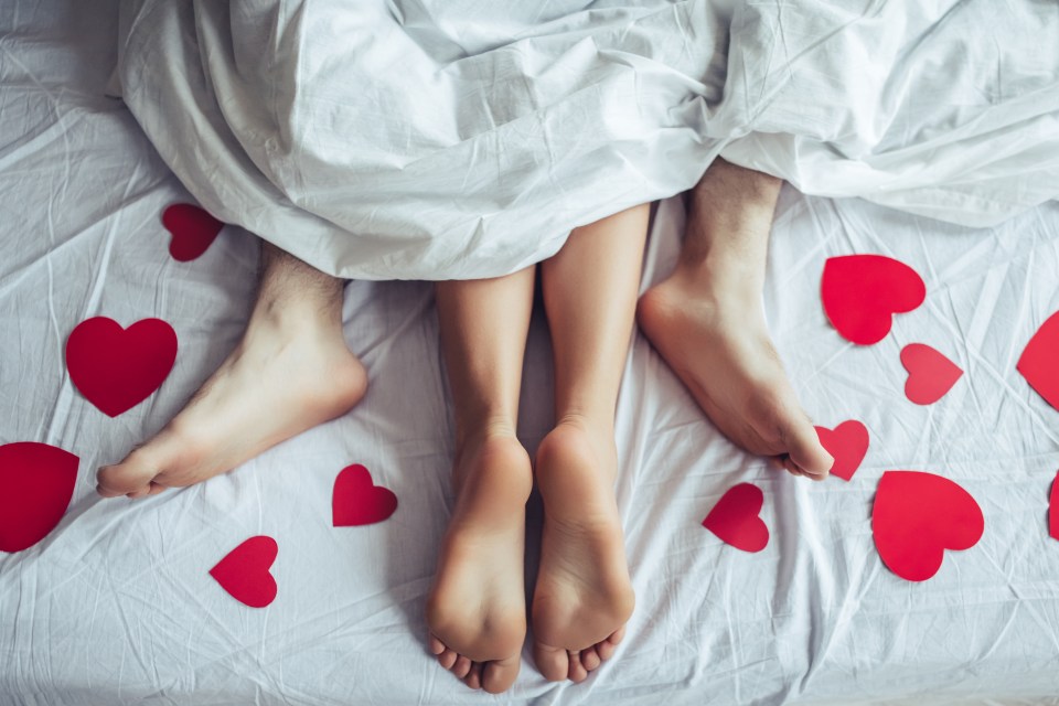 Couple's feet under a blanket with red paper hearts.