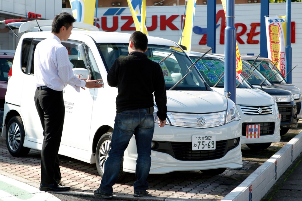 A salesperson shows a customer a Suzuki car at a dealership.