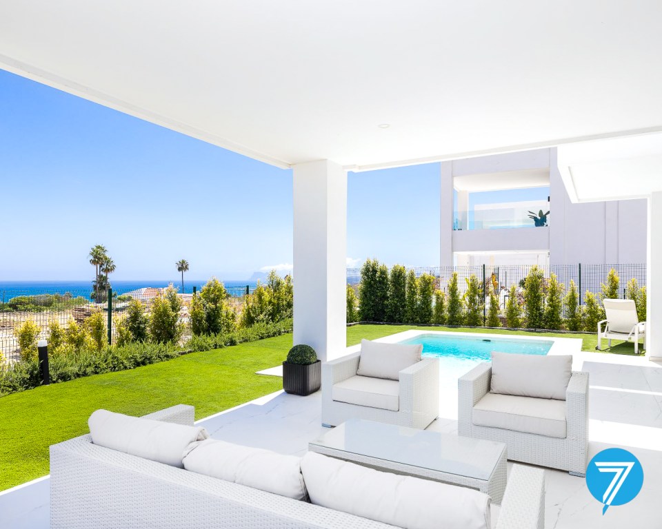 Ocean view from a modern patio with white furniture and a pool.