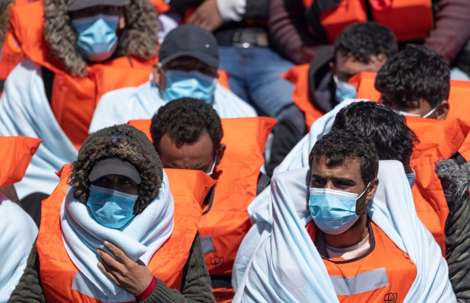 Migrants in life vests being guided to a holding facility.