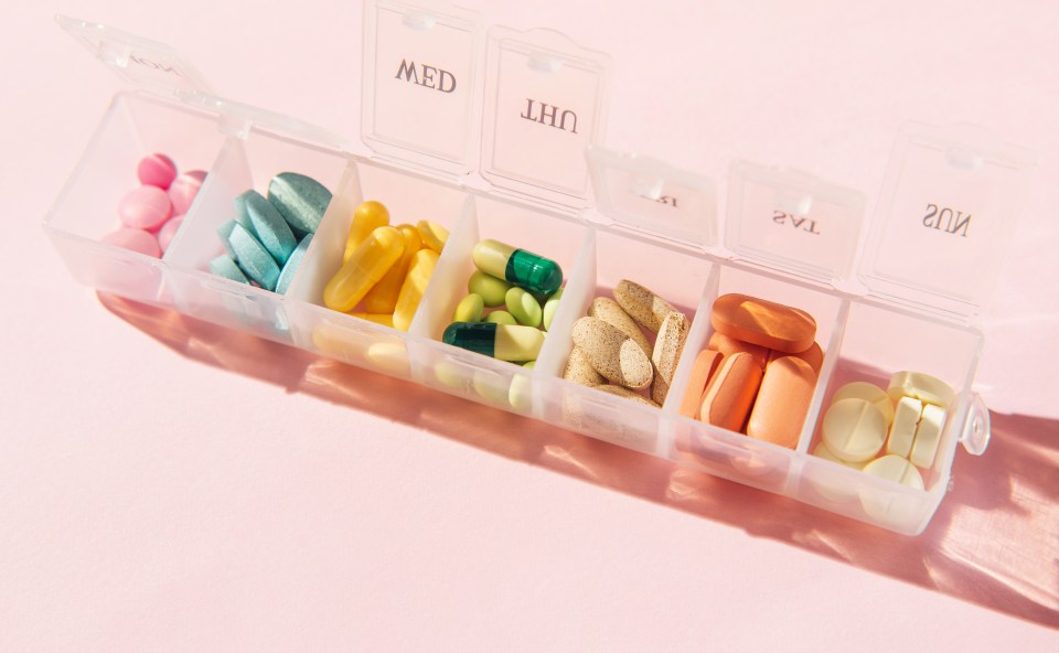 Box for pills and capsules on pink background. Pills organizer with tablets, vitamins, painkillers, medications and dietary supplements. Minimal medical, health care, pharmacology concept. Flat lay, top view.