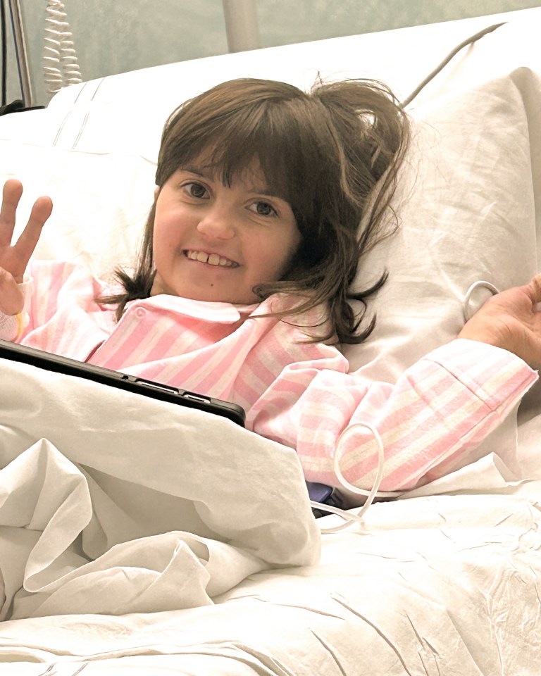 Smiling girl in a hospital bed using a tablet.