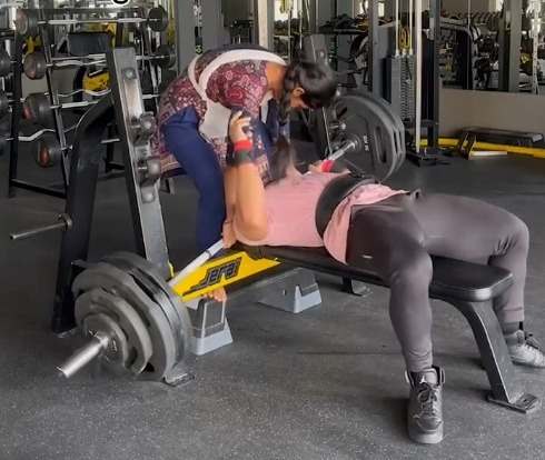 A woman assists a man bench pressing 165kg in a gym.