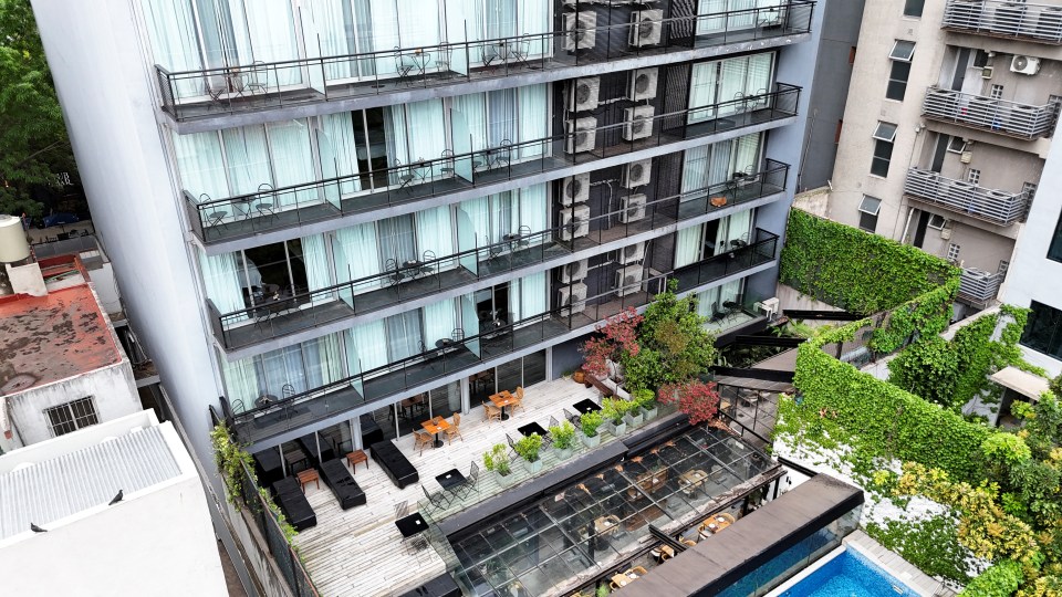 Drone view of a hotel with balconies, a rooftop patio, and a pool.