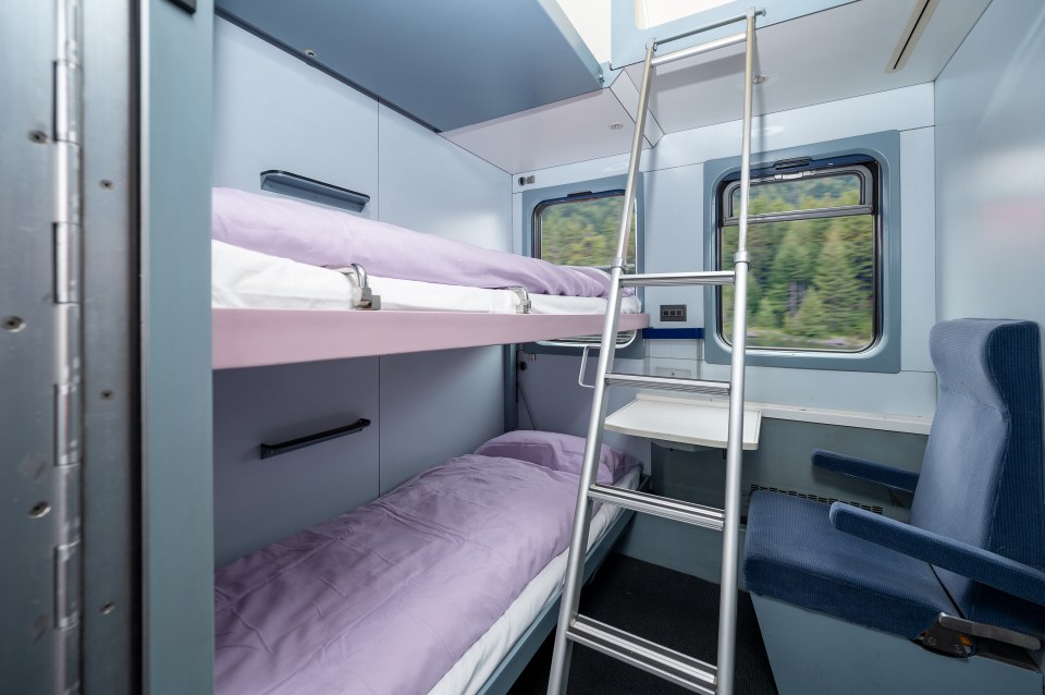 Train sleeper car with bunk beds and a seat.