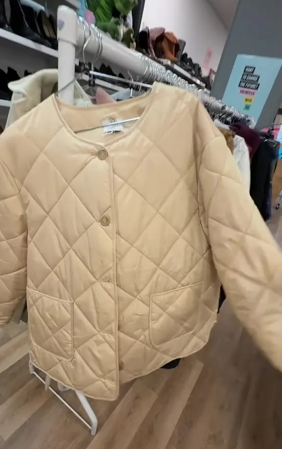 Beige quilted jacket on a hanger in a charity shop.