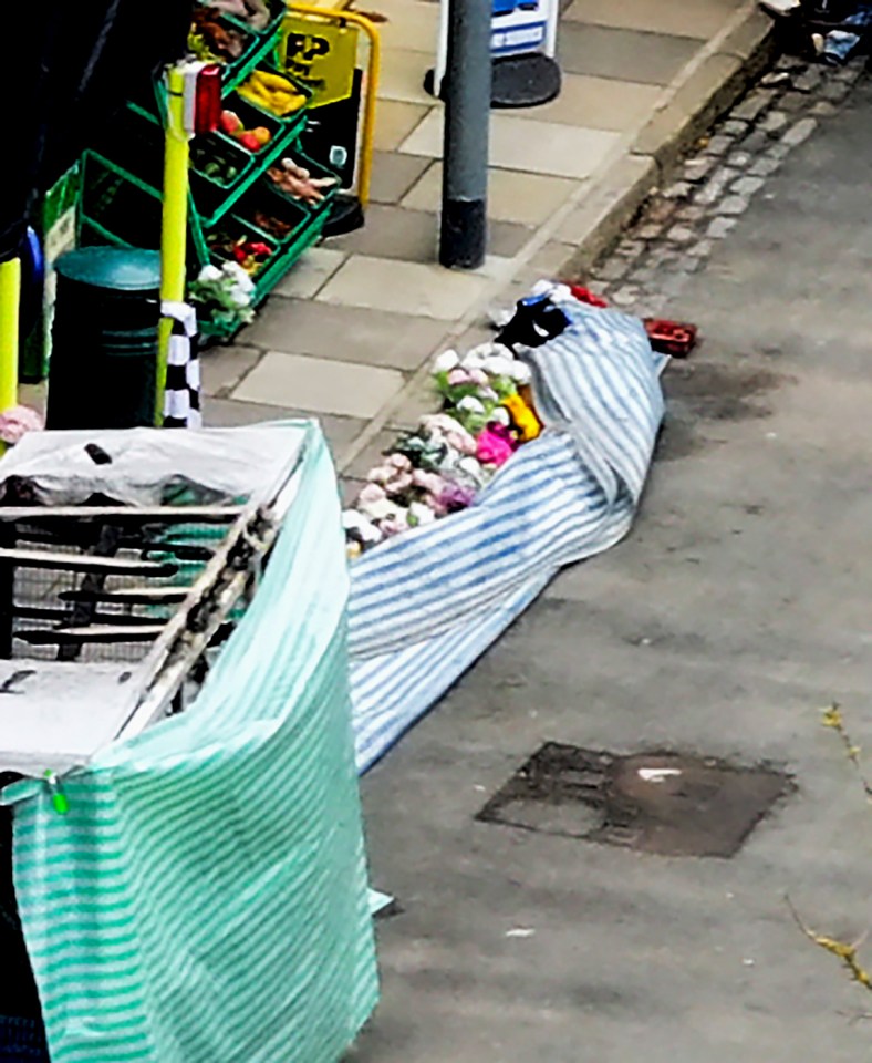 Flowers and a covered market stall near a damaged building after a car crash.