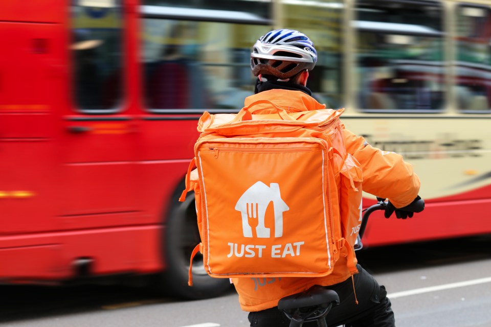 A Just Eat delivery person on a bicycle waits to cross the street.