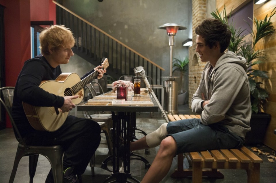 Ed Sheeran playing guitar for a young man with a leg injury.