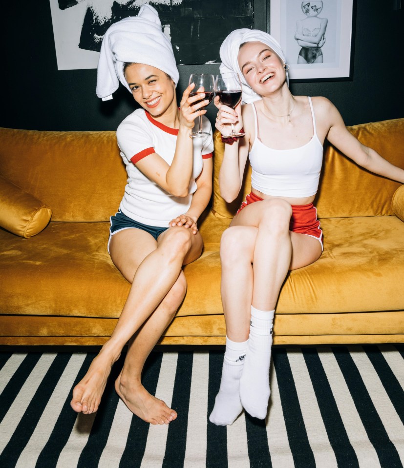 Two women in bathrobes relaxing on a couch, drinking wine.