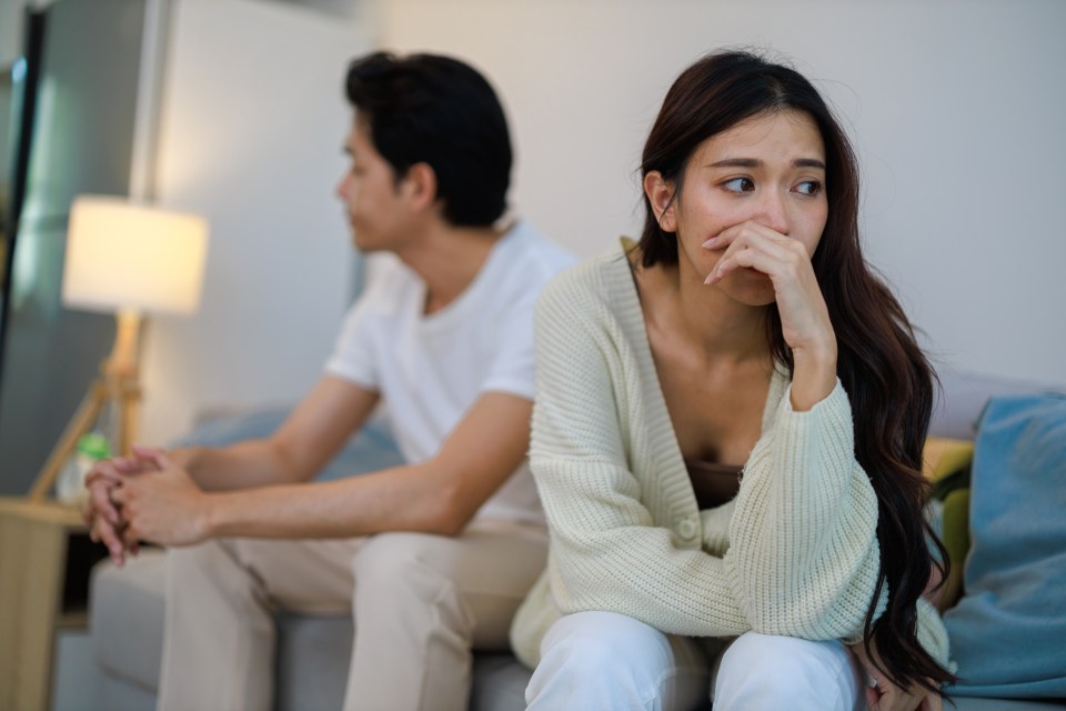 Upset Asian couple sitting on a couch, ignoring each other.