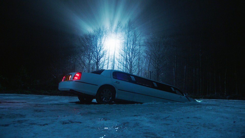 Limousine partially submerged in a frozen lake at night.