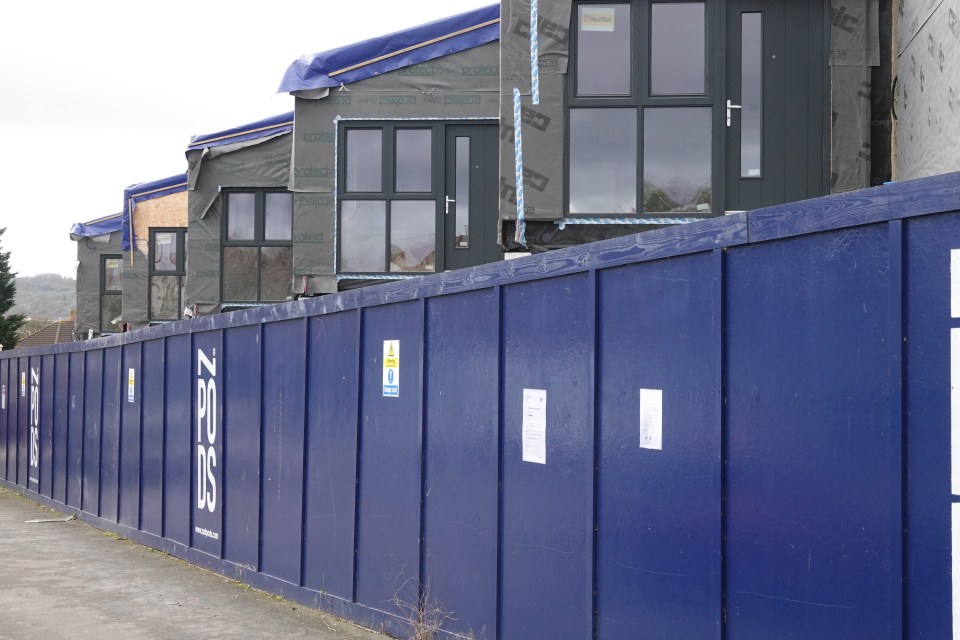 Construction of ZPods housing units behind a blue security fence.