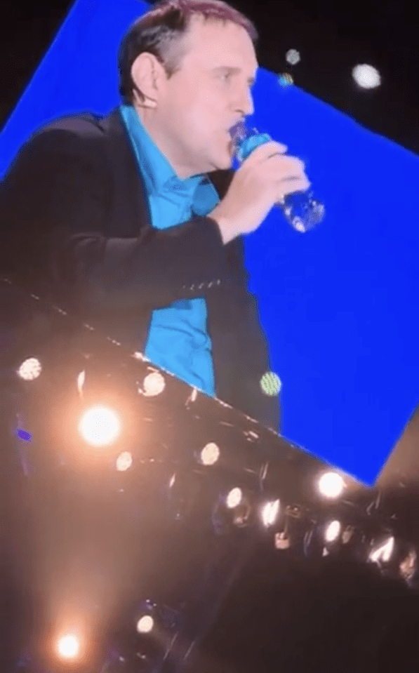 Peter Kay drinking water onstage.