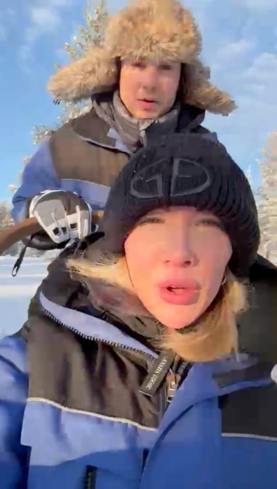 Woman in a winter hat being pulled on a sled by a man in a fur hat.