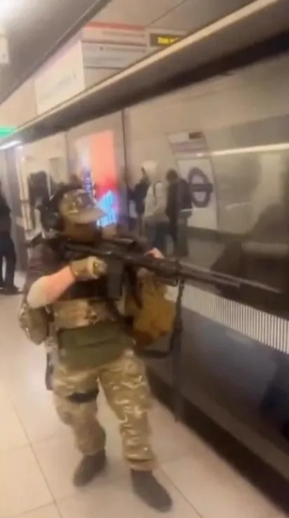 Person in tactical gear holding a rifle on a subway platform.