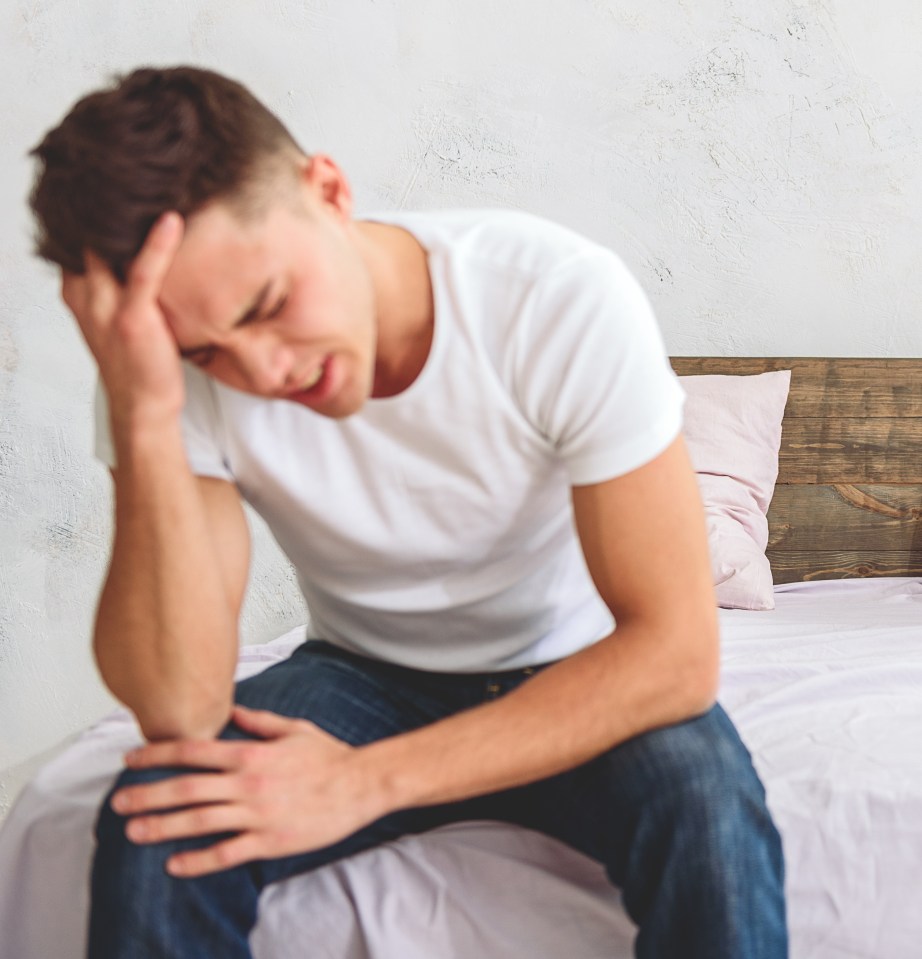 A young gay couple sitting on a bed, one crying while the other looks away.