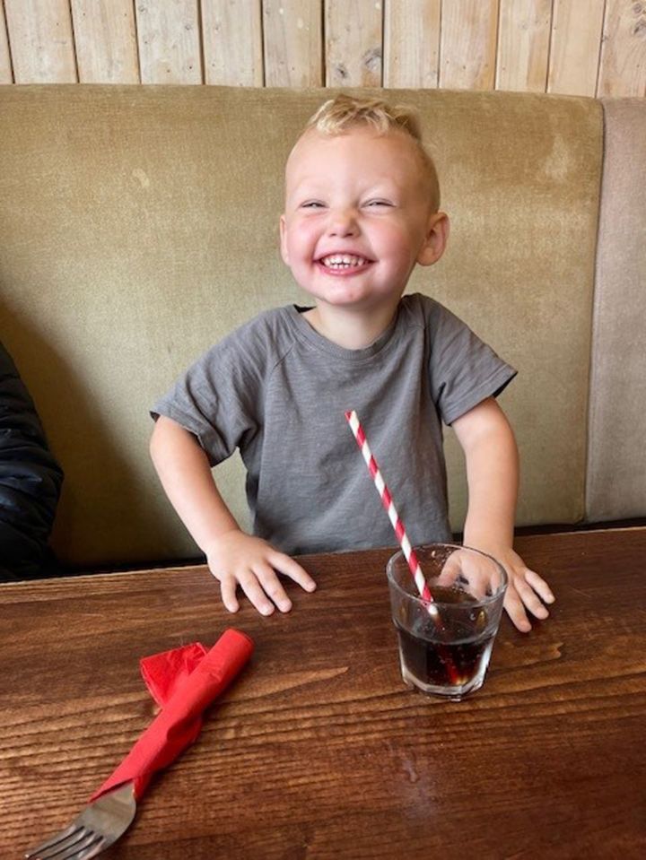 Smiling toddler sitting at a table with a drink.