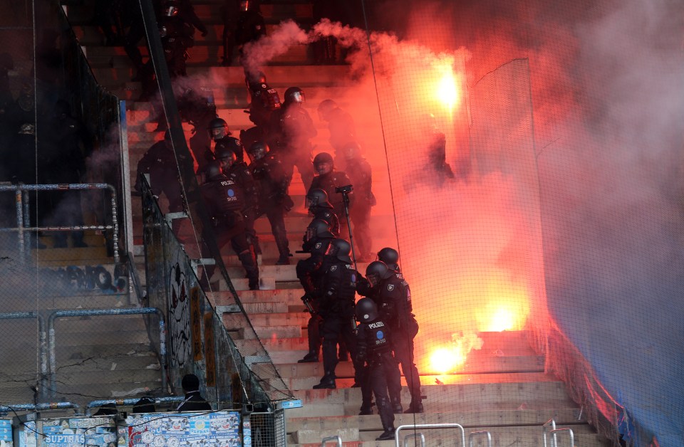 Police officers confronting fans throwing flares at a soccer match.