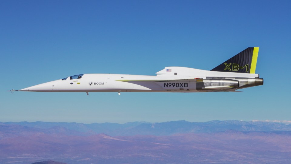 XB-1 supersonic jet in flight over mountains.