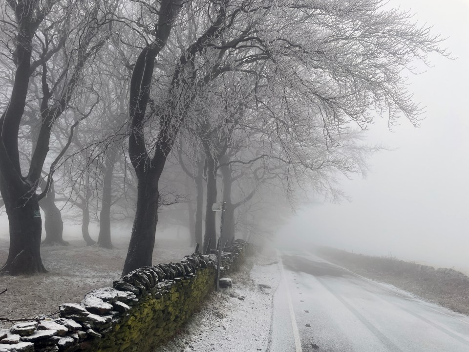 Foggy road in High Bradfield, near Sheffield, with snow-covered trees and a stone wall.