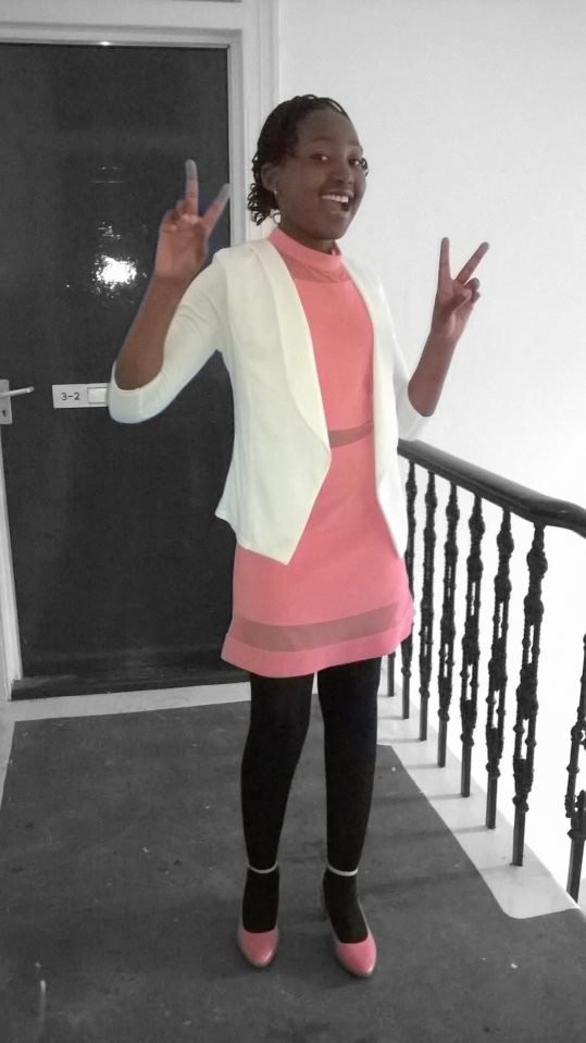 Photo of a young woman in a pink dress and white jacket making peace signs.