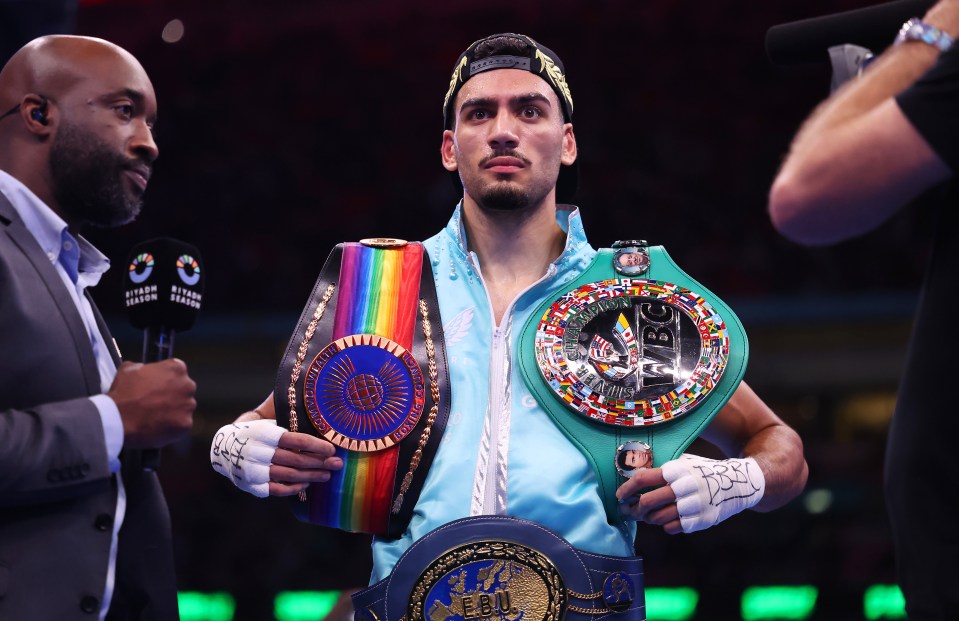 Hamzah Sheeraz celebrates a boxing victory, holding three championship belts.