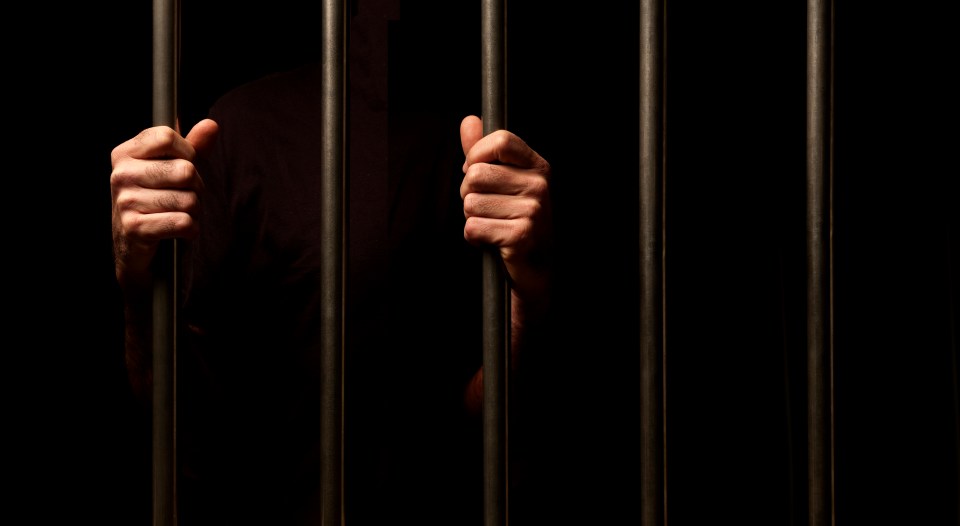 Prisoner's hands gripping prison bars.