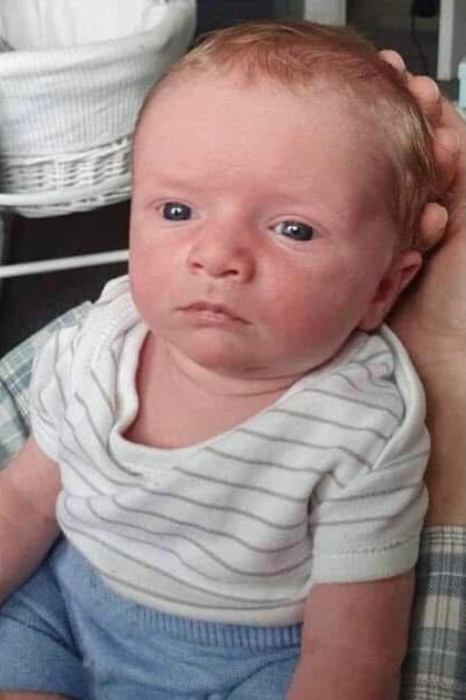 Photo of a baby wearing a striped shirt and blue shorts.