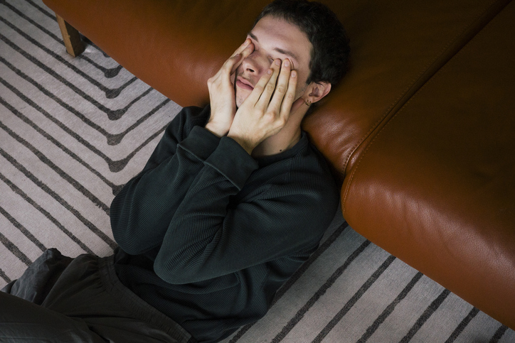 Man lying on the floor with his face in his hands.