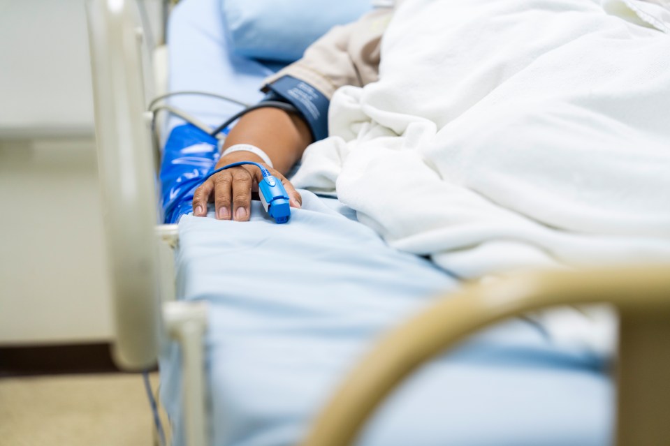 A male patient sleeping in a hospital bed with a heart rate monitor attached to his finger.