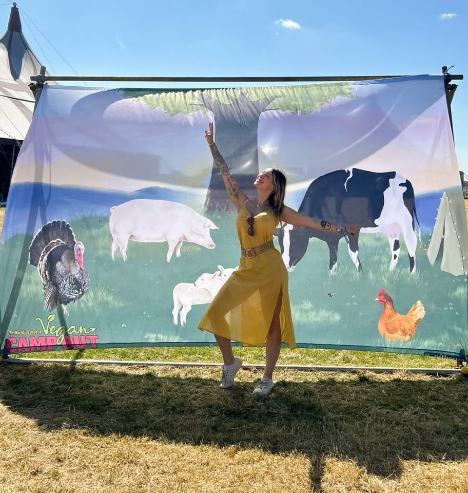 Woman in yellow dress posing in front of a banner depicting farm animals at the Vegan Campout.