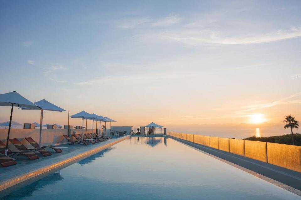 Sunrise over rooftop infinity pool with lounge chairs and umbrellas.