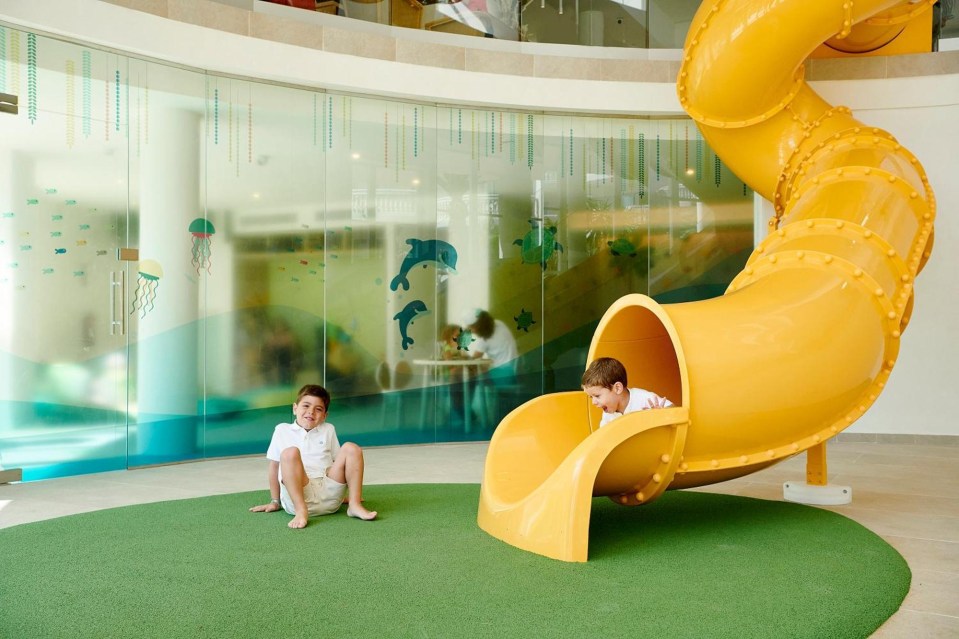 Two boys playing on a yellow slide in a children's play area.