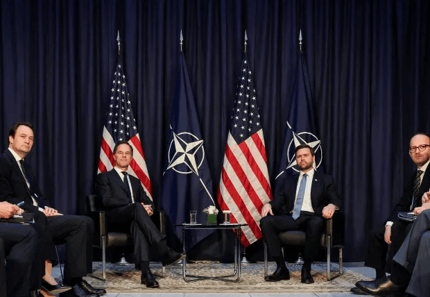 Five men seated in front of US and NATO flags.