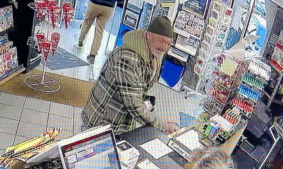 Surveillance image of a man in a plaid shirt and beanie at a store counter.